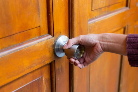 a person's hand on a door knob to open a brown wooden door