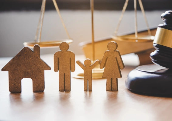 Wooden cutouts of a house, parents, and child placed beside a judge’s gavel and scales of justice, symbolising family law and custody decisions.