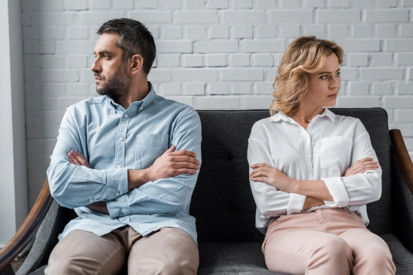 Man and woman sitting on a couch with arms crossed, looking away from each other in disagreement.
