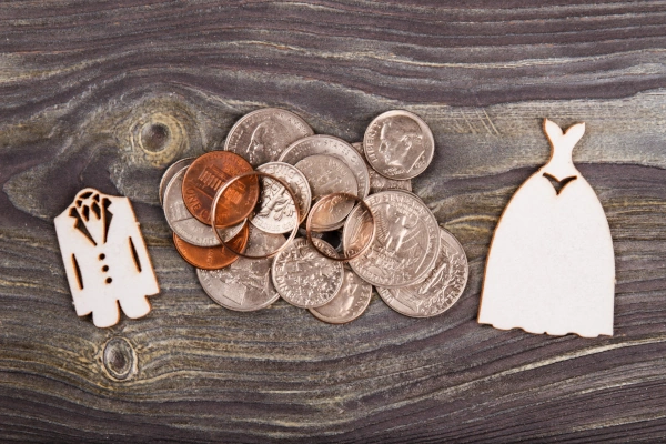 Wooden cutouts of a groom’s suit and a bride’s dress separated by a pile of coins and wedding rings, symbolising the financial division in divorce.